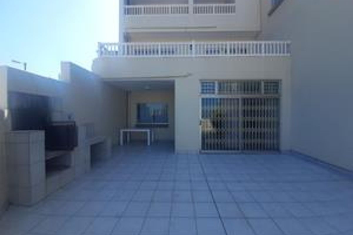 Rear exterior view of the townhouse featuring a paved patio area with a built-in braai and access to the ground floor living space.