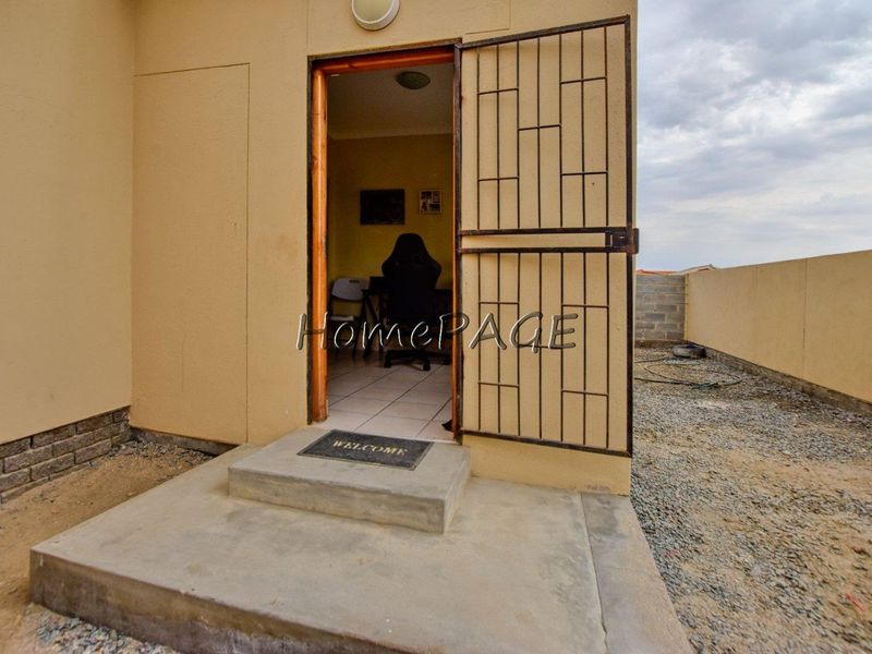 Rear exterior view showing a doorway with a security gate, concrete step, and unfinished ground area.