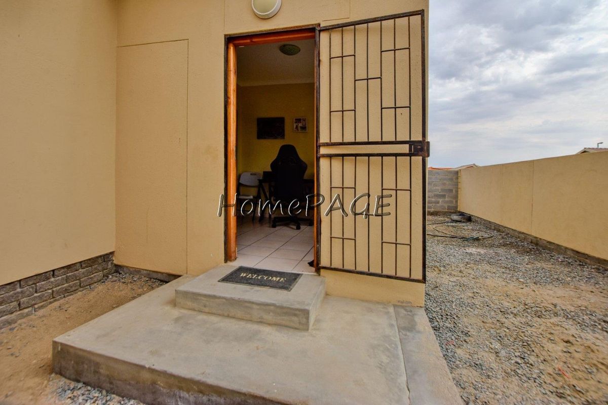 Rear exterior view showing a doorway with a security gate, concrete step, and unfinished ground area.
