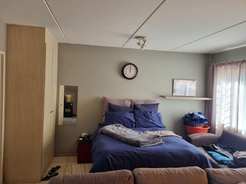 A bedroom featuring tiled flooring, a built-in wardrobe, and a floating shelf. The room has a neutral wall finish and ceiling lighting.
