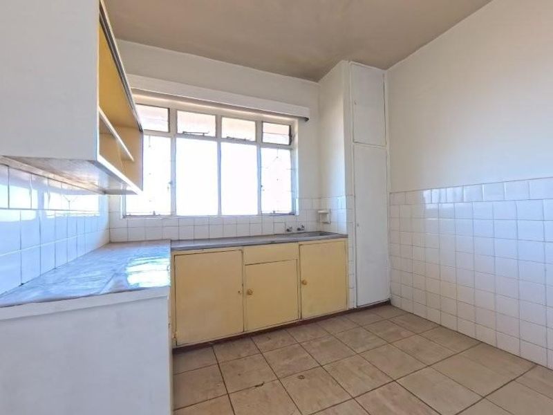 A dated, empty kitchen featuring tiled walls, built-in cabinetry, and tiled flooring, offering a blank canvas for a modern renovation.