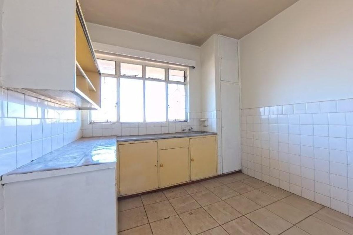 A dated, empty kitchen featuring tiled walls, built-in cabinetry, and tiled flooring, offering a blank canvas for a modern renovation.