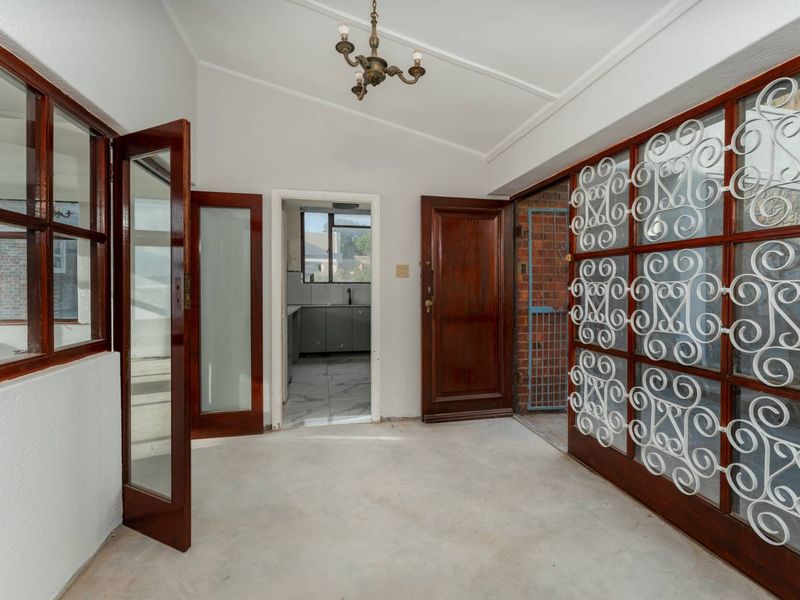 An entrance area featuring timber-framed glass doors, a decorative security grille, and a vaulted ceiling, leading through to a kitchen space.