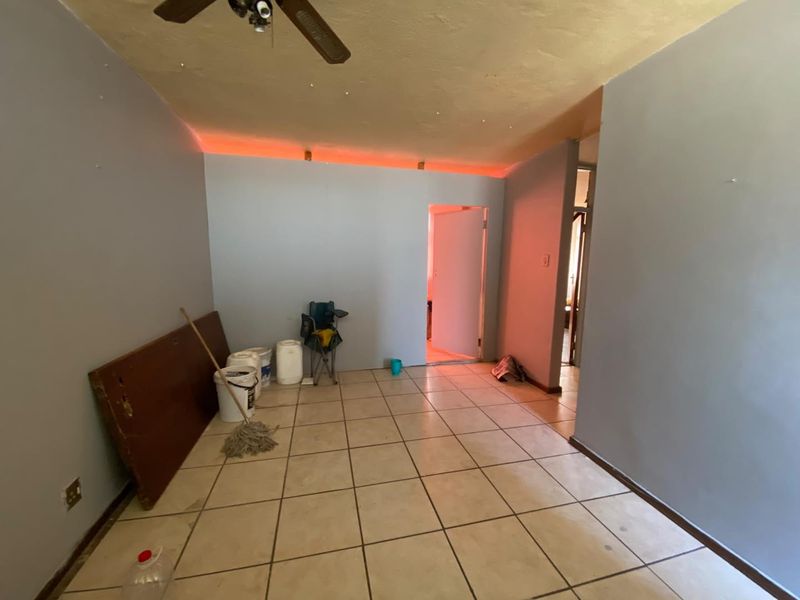 An empty living area featuring ceramic floor tiles, a ceiling fan, and decorative recessed lighting, presenting a blank canvas for renovation.