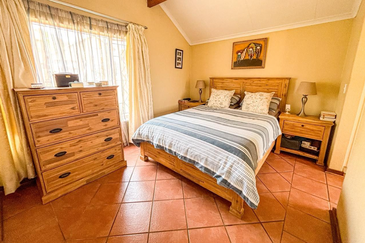 A cozy bedroom featuring a vaulted ceiling, terracotta floor tiles, and natural light through a window with security bars.