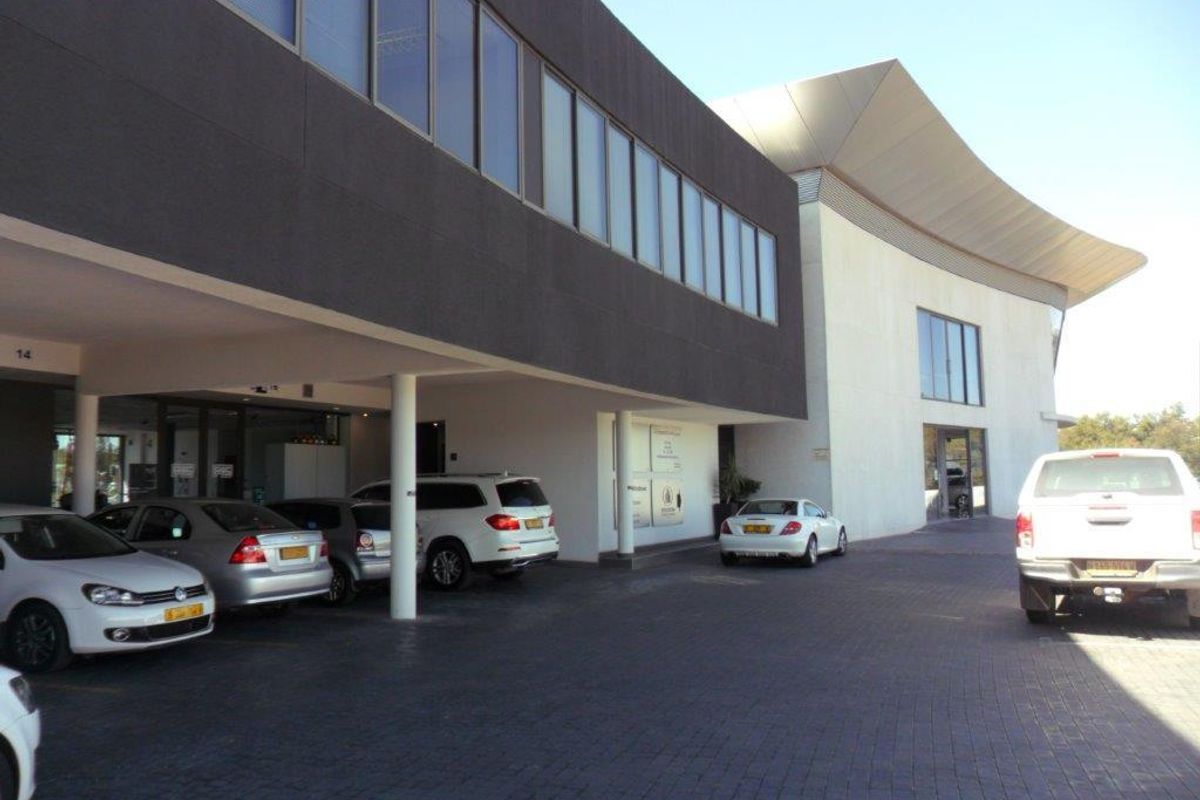 Modern office building exterior featuring a paved driveway, covered parking area, and distinctive architectural design with large glass windows and a curved roof.
