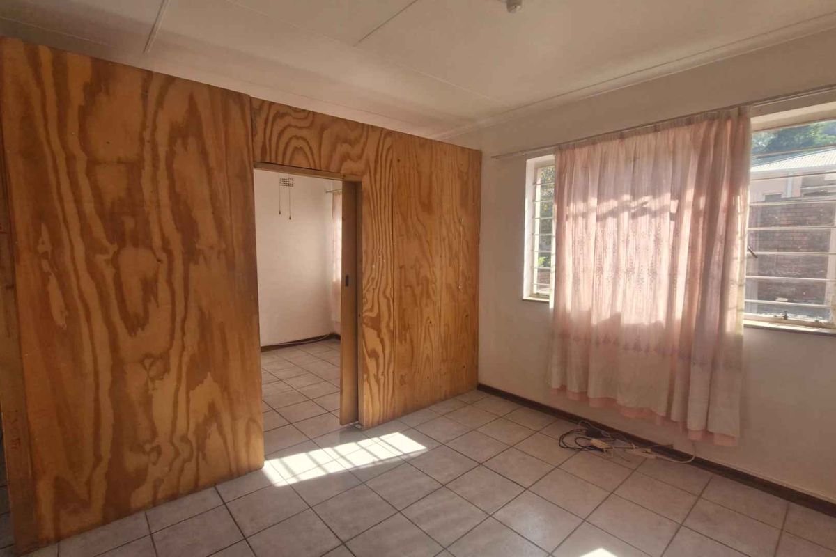 A living area featuring tiled flooring and a prominent plywood partition wall, offering a blank canvas for renovation and modernization.