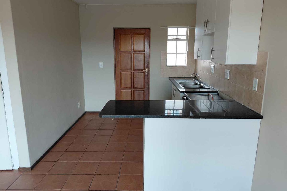 A functional kitchen featuring granite countertops, built-in cabinetry, a stainless steel sink, and tiled flooring in a neutral, open-plan layout.