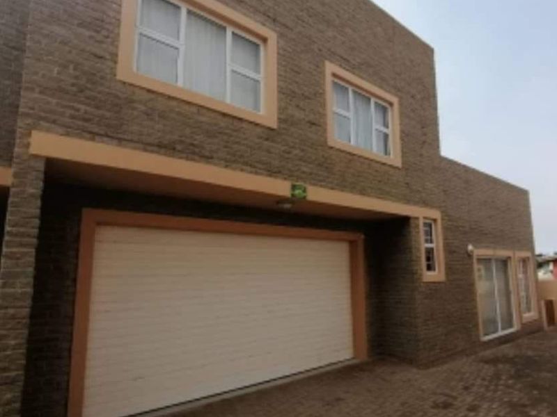 Front elevation of a modern townhouse featuring a double garage, textured brick facade, and paved driveway access.