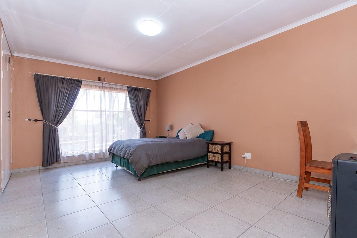 A spacious bedroom featuring neutral wall tones, large windows with curtains, and tiled flooring throughout.