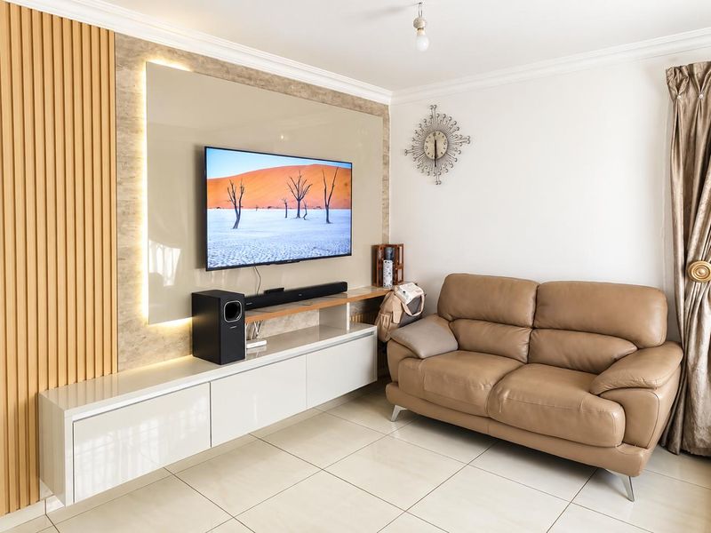 Modern living room featuring a custom built-in media unit with integrated LED lighting, slatted timber wall accents, and polished tiled flooring.
