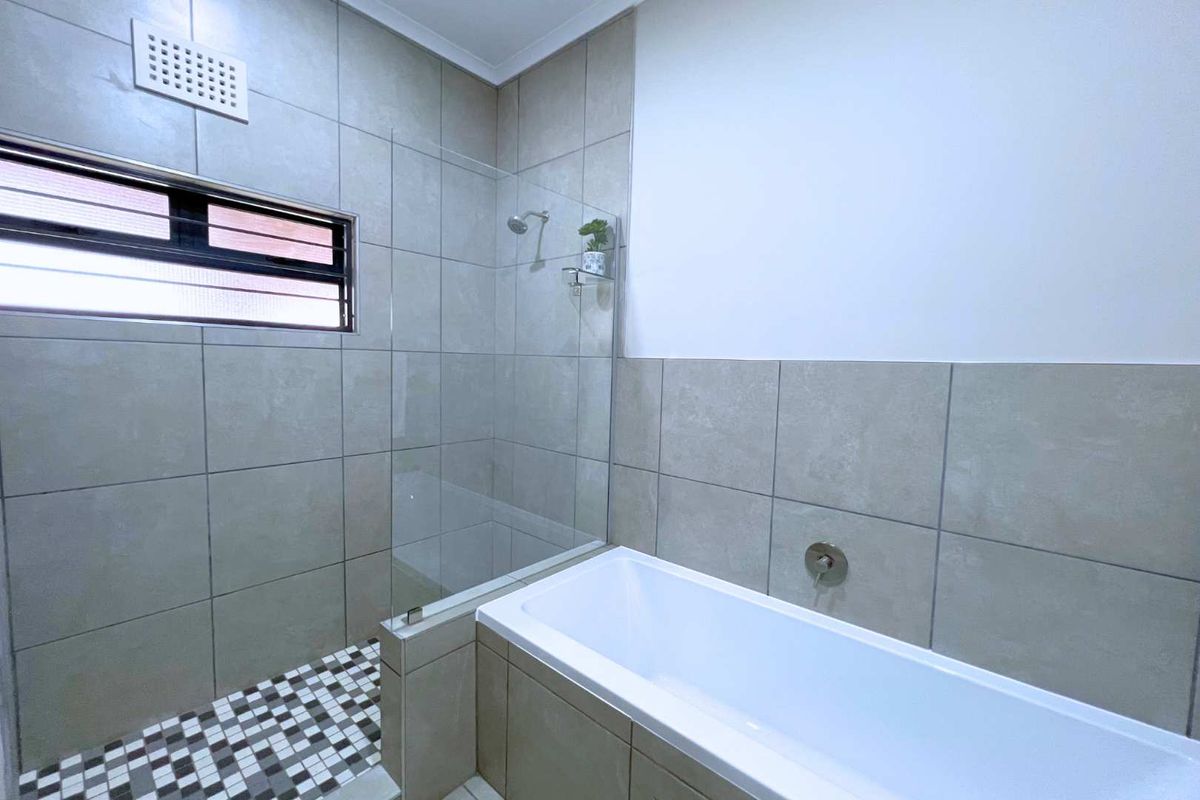 Modern bathroom featuring a tiled shower enclosure with a glass screen, a built-in bathtub, and neutral wall tiling.