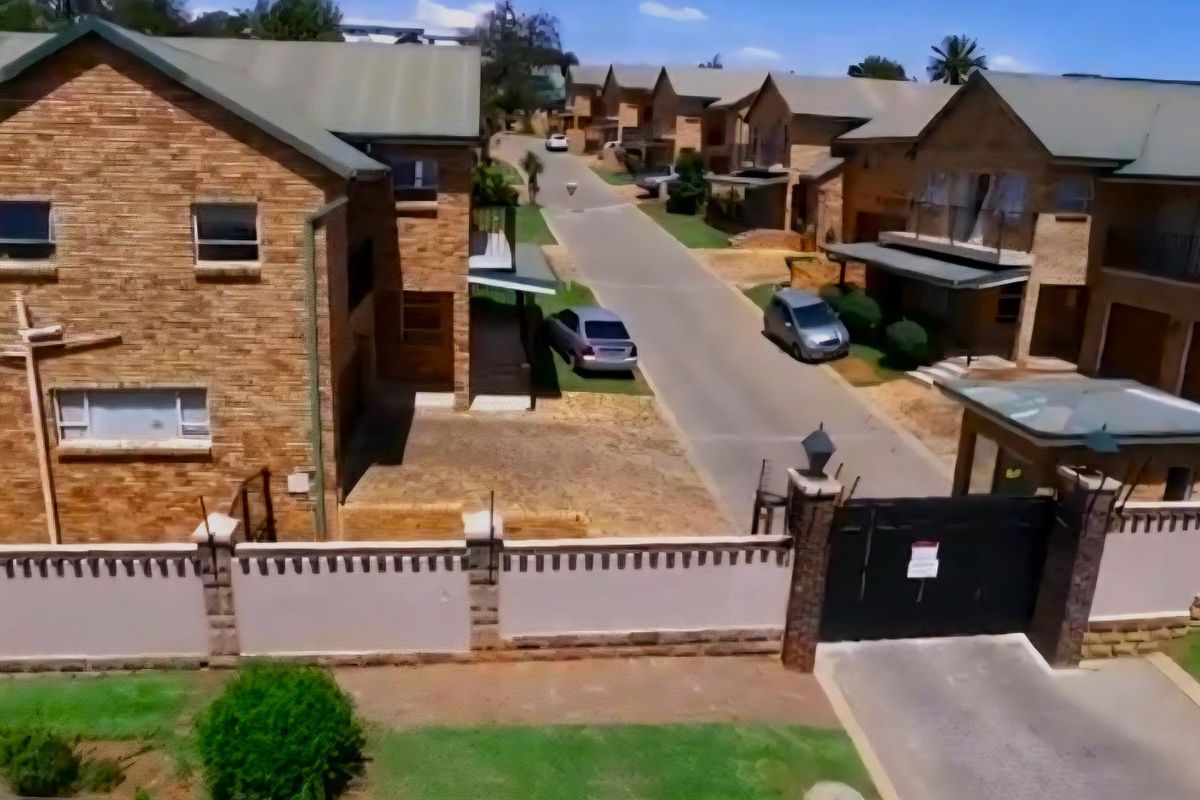 Aerial view of a cluster housing complex featuring brick facades, paved internal roads, and a secure gated entrance.