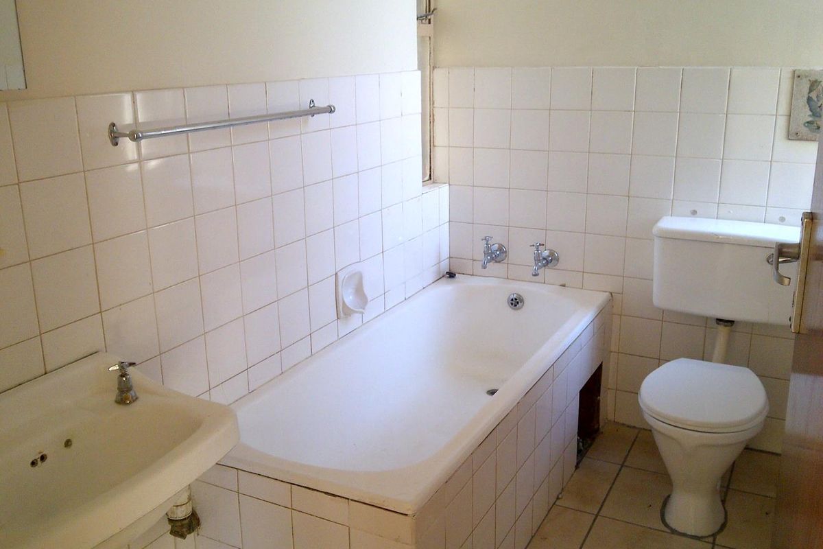 A dated bathroom featuring a standard bathtub, pedestal sink, and toilet with white wall tiling throughout.