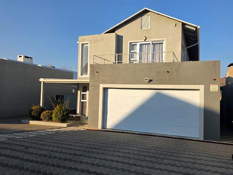 Front view of a modern two-story house featuring a double garage, paved driveway, and an upper-level balcony.