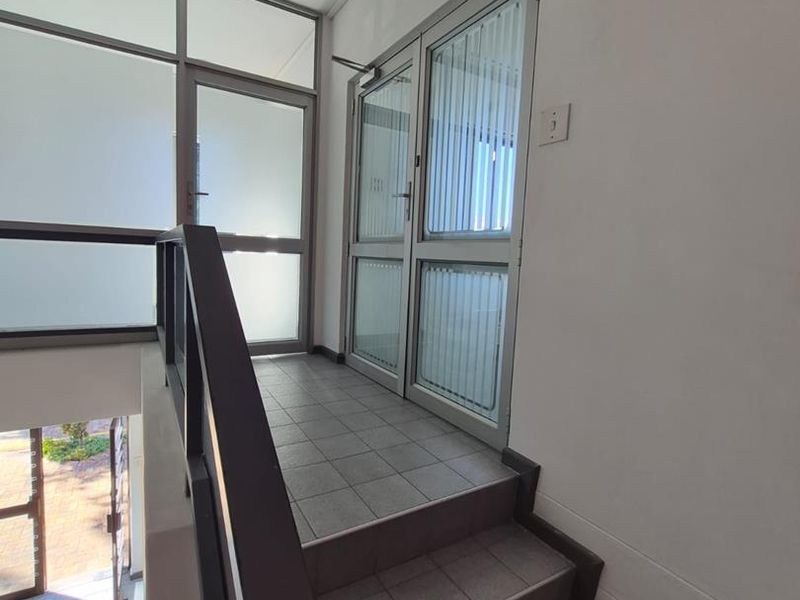 A bright office entrance area featuring a tiled staircase, aluminium-framed glass doors, and large windows providing natural light.