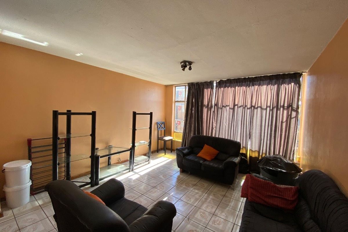 A living room area featuring tiled flooring and natural light through large windows, requiring cosmetic updates to the wall finishes.