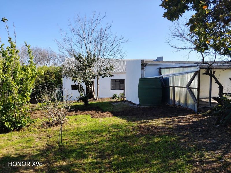 Rear view of the property featuring a garden area, water storage tank, and a corrugated metal lean-to structure.