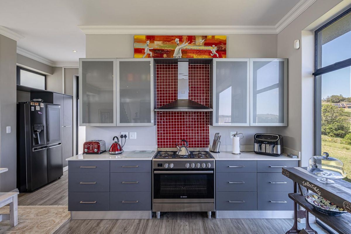 Modern kitchen featuring grey cabinetry, a stainless steel gas stove with extractor fan, and a vibrant red tiled backsplash.
