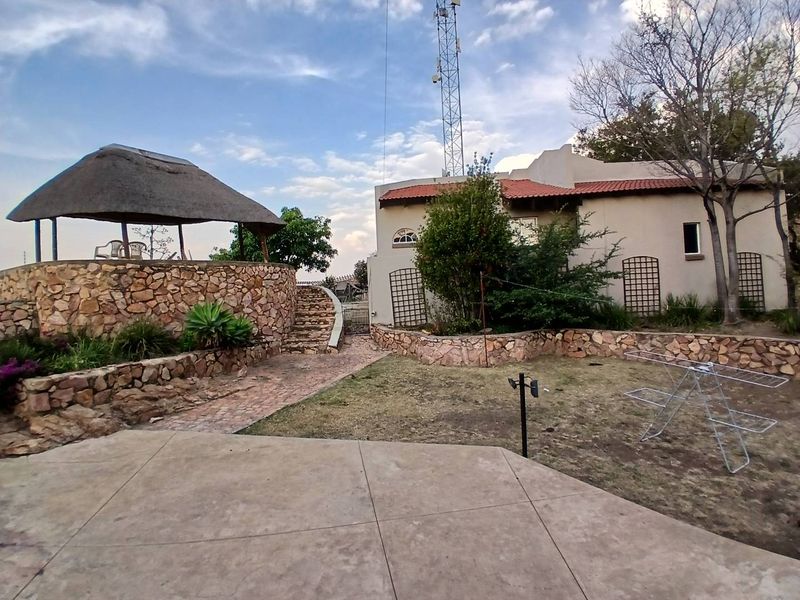 Rear garden area featuring a thatched gazebo, stone retaining walls, a paved patio, and a stone staircase leading to the elevated structure.