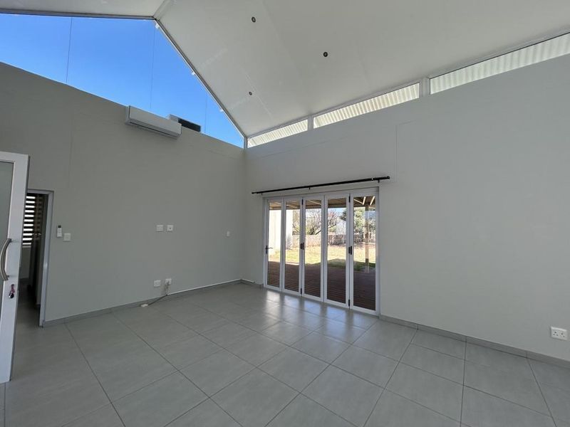Spacious living area featuring high vaulted ceilings, clerestory windows for natural light, modern tiled flooring, and bi-fold doors opening to the outdoor space.