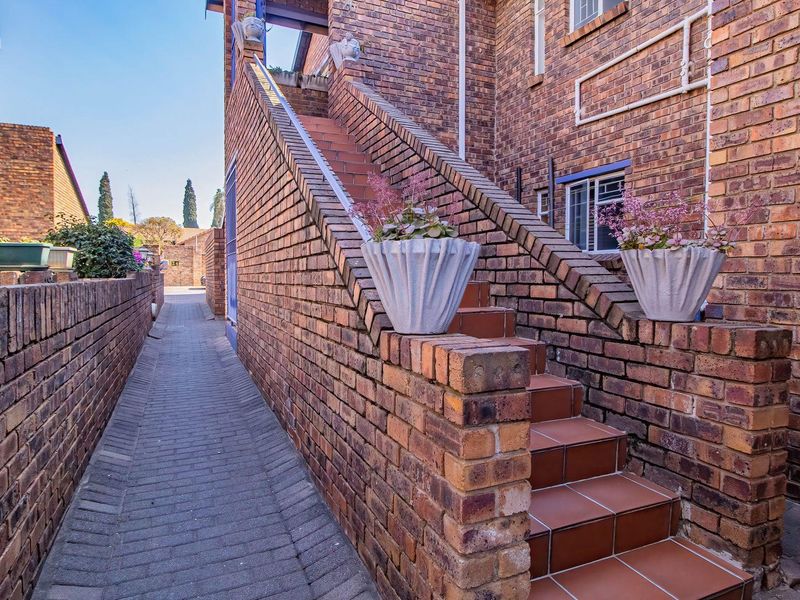 Exterior view of an apartment building featuring a brick facade, a tiled staircase, and a paved walkway leading to the rear entrance.