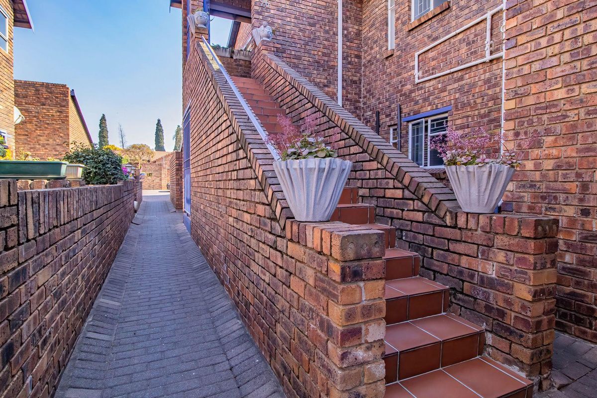 Exterior view of an apartment building featuring a brick facade, a tiled staircase, and a paved walkway leading to the rear entrance.