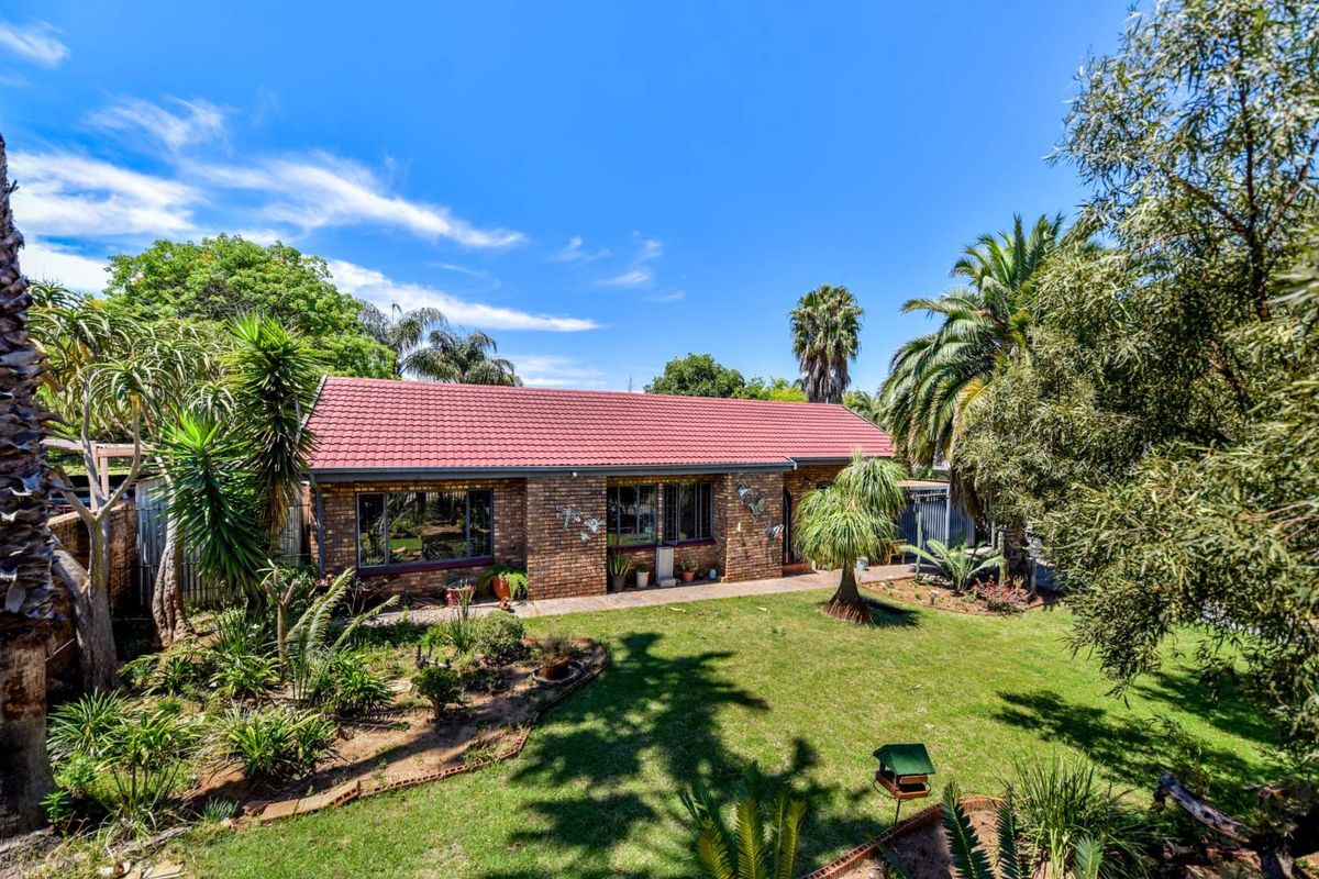 A well-maintained brick house featuring a tiled roof, set within a lush, established garden with a paved walkway.