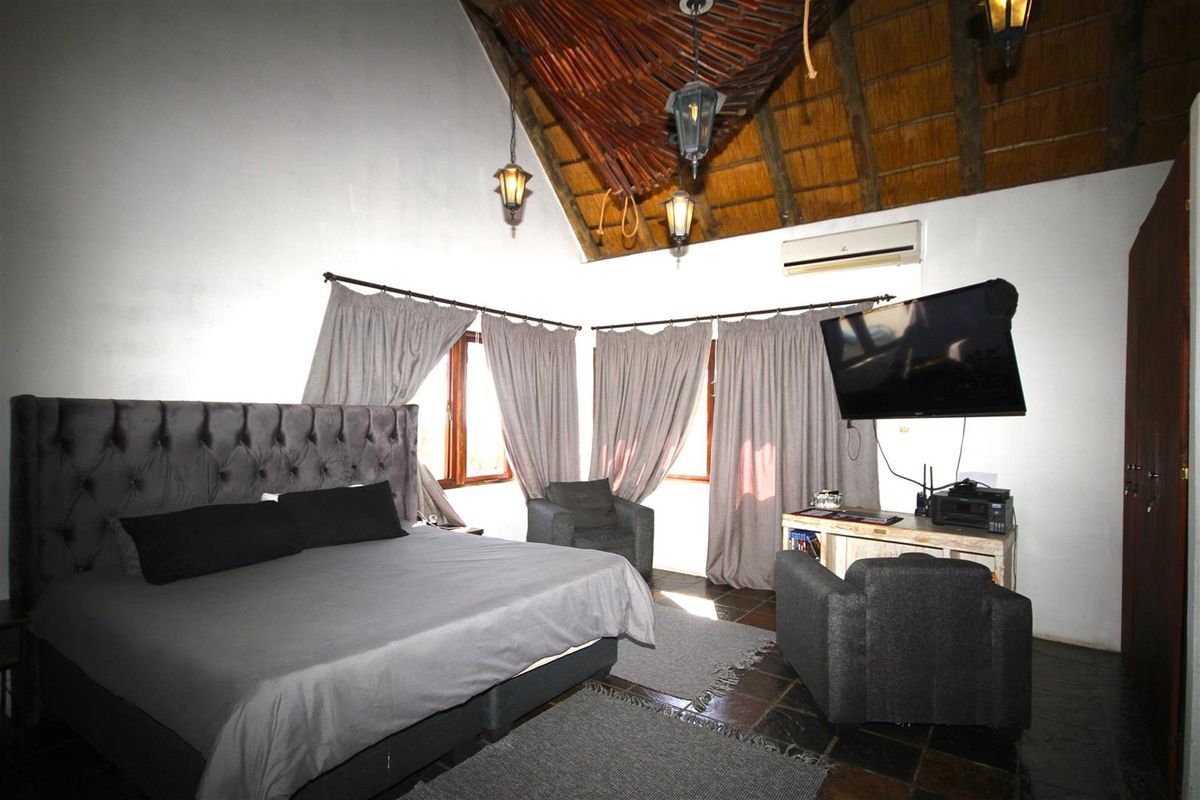Spacious bedroom featuring a high vaulted thatched ceiling, exposed timber beams, tiled flooring, and a wall-mounted air conditioning unit.