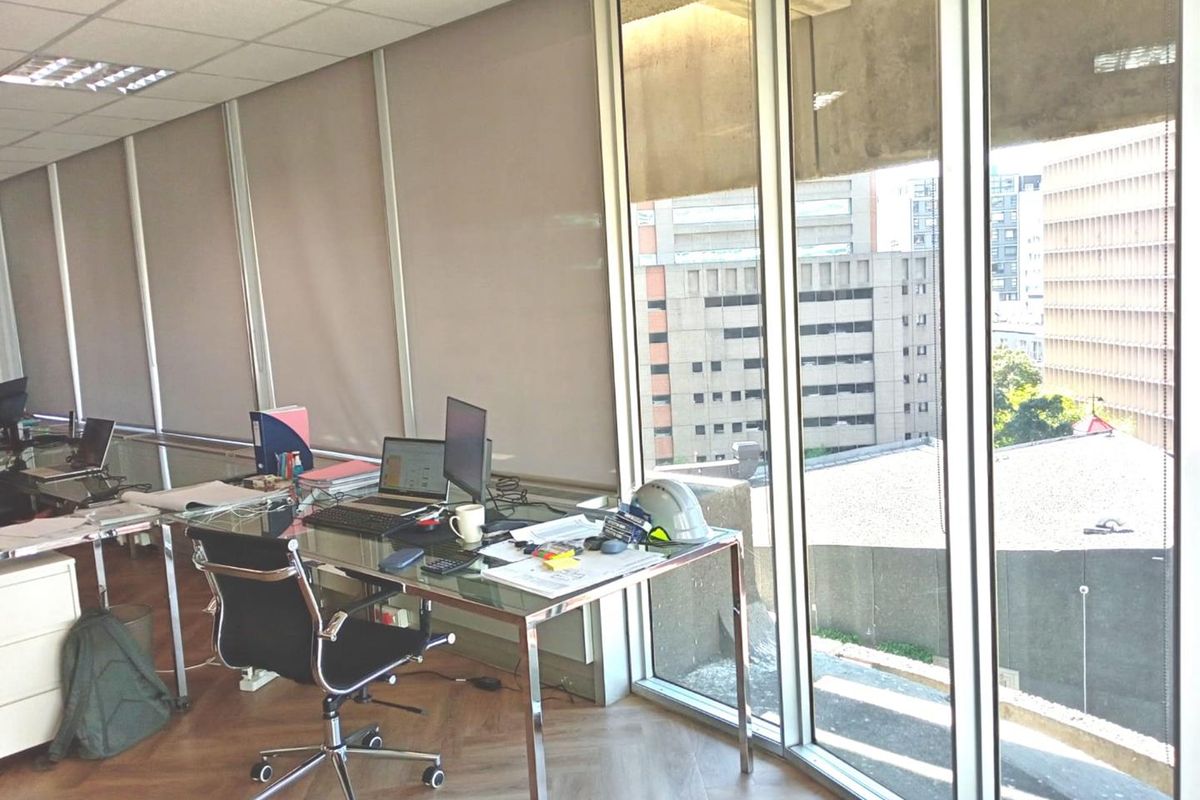 A bright office space featuring parquet flooring, suspended ceilings, and expansive floor-to-ceiling windows offering an urban city view.