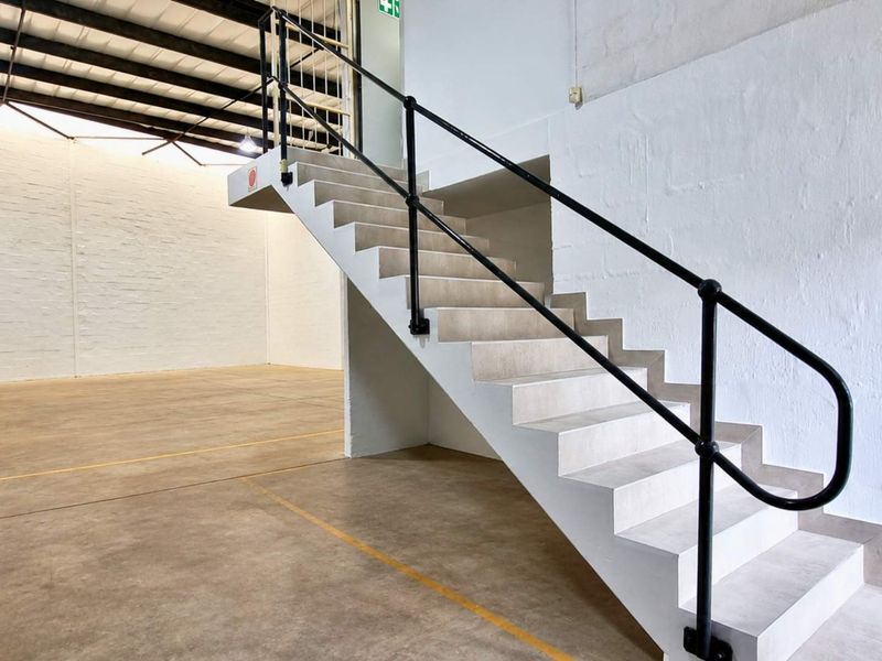 Spacious industrial utility area featuring a concrete staircase with metal handrails, exposed steel roof trusses, and durable concrete flooring.