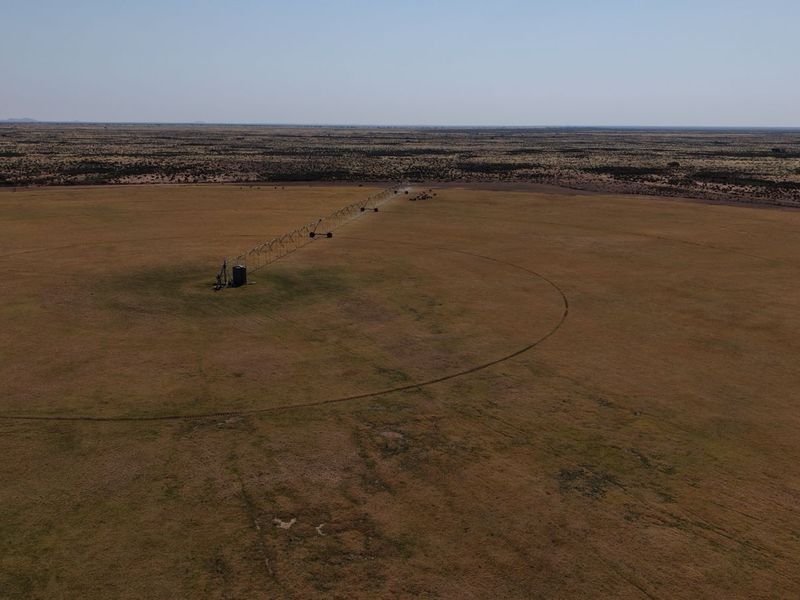 Aerial view of a large agricultural field featuring a center pivot irrigation system set against a vast rural landscape.