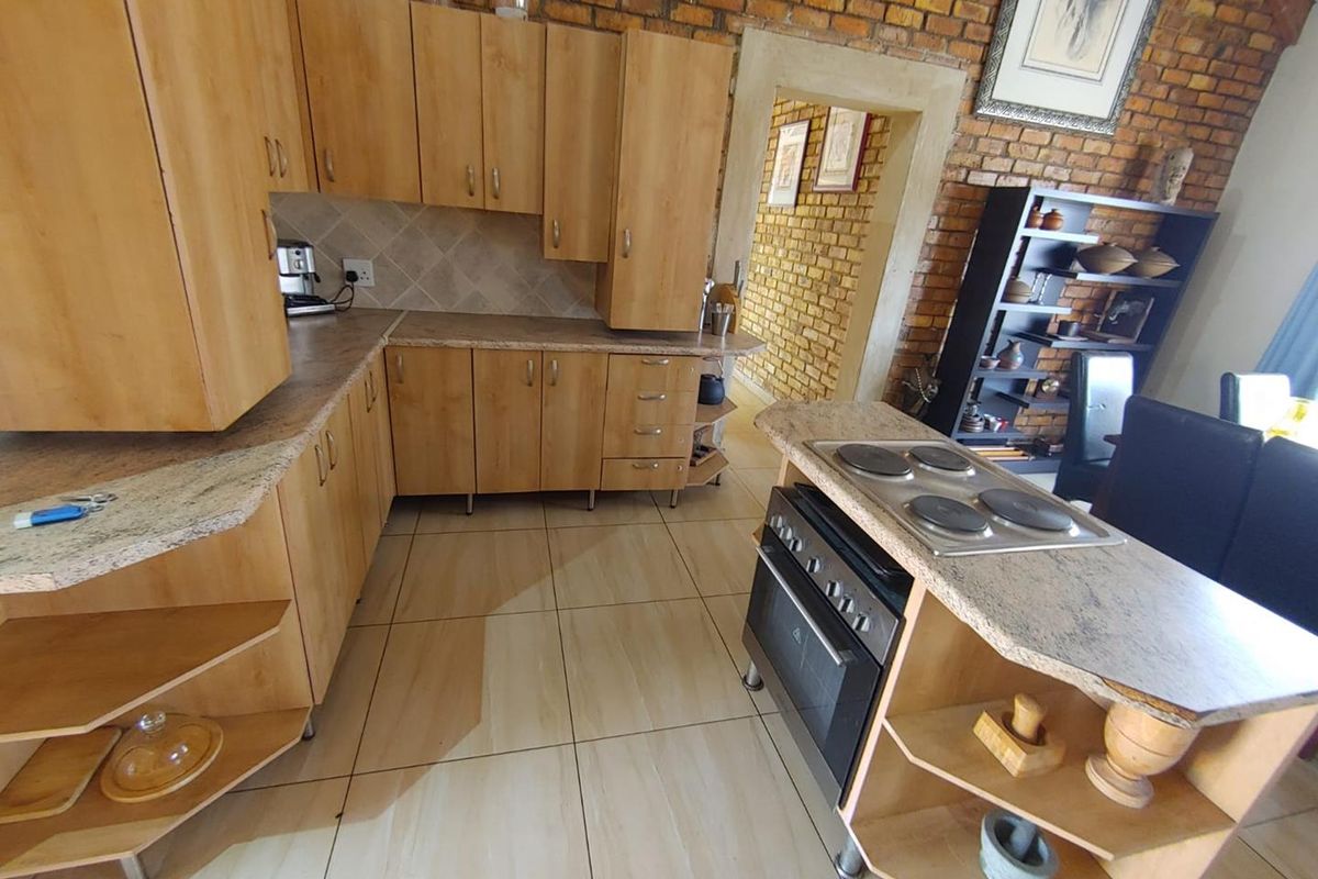 Kitchen featuring light wood-look cabinetry, stone-effect countertops, a built-in oven with hob, and a rustic exposed brick feature wall.