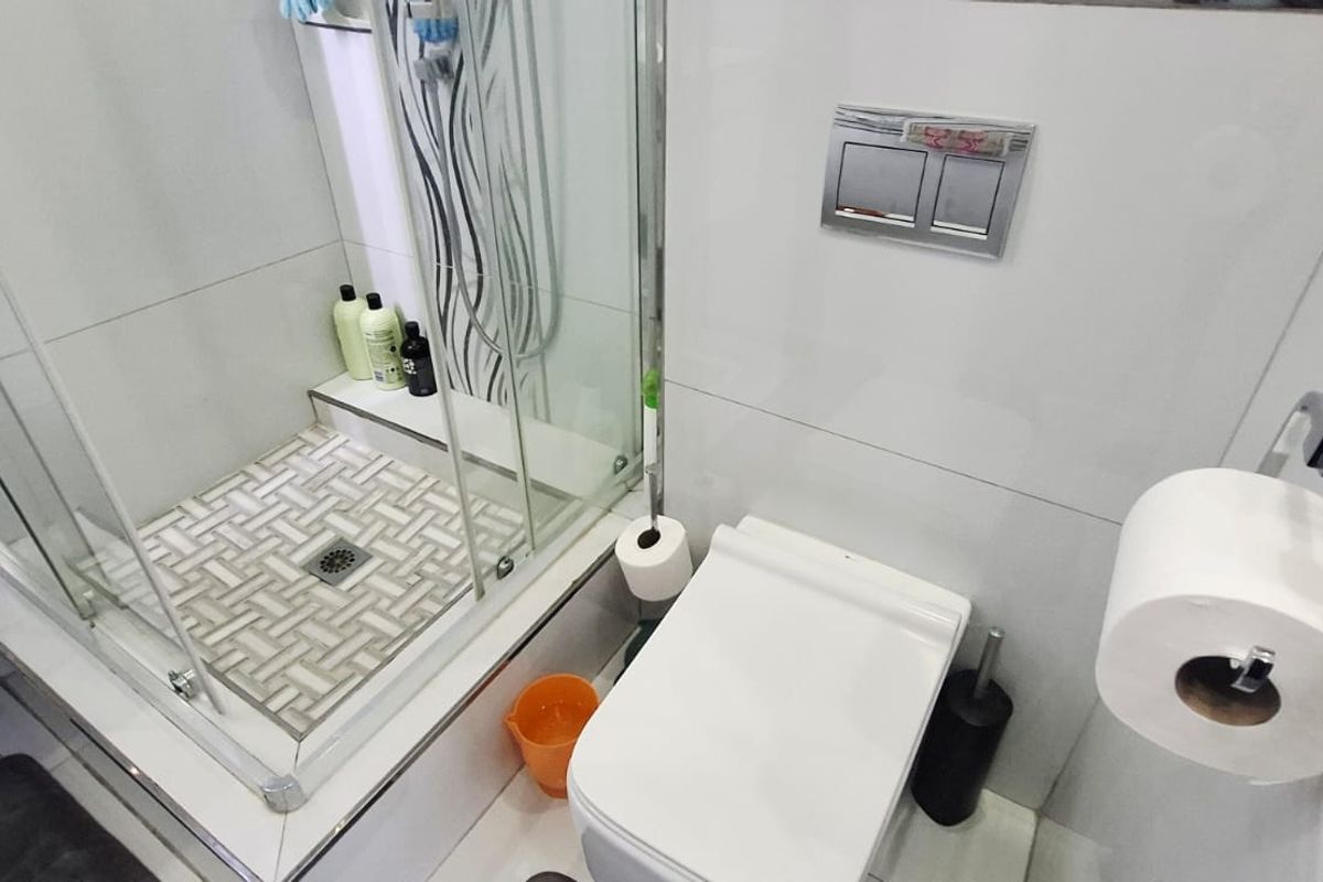A compact modern bathroom featuring a glass-enclosed shower with decorative mosaic floor tiling and a wall-mounted toilet with a chrome flush plate.