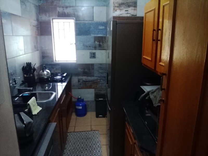 A compact kitchen featuring wooden cabinetry, granite countertops, a gas hob, and decorative tiled wall finishes.