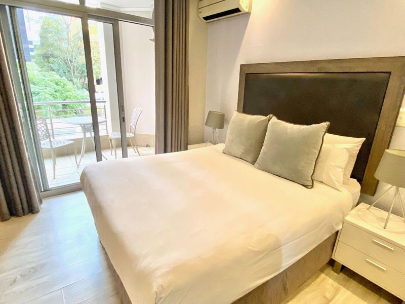 A well-maintained bedroom featuring light-toned tiled flooring, an integrated air conditioning unit, and direct access to a private balcony through sliding glass doors.