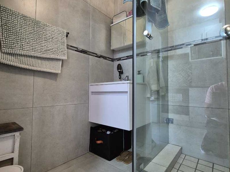 Modern bathroom featuring large-format grey wall and floor tiles, a wall-mounted vanity, and a glass-enclosed shower with a tiled base.