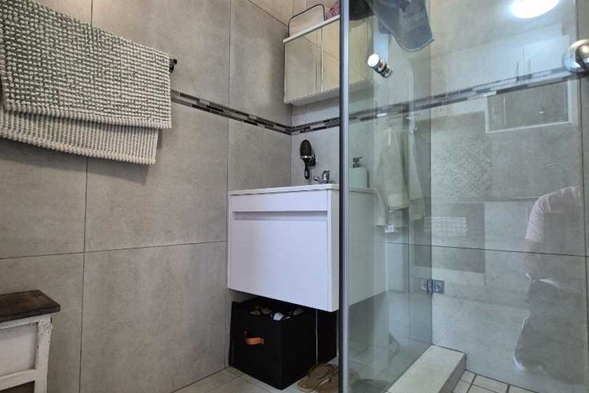 Modern bathroom featuring large-format grey wall and floor tiles, a wall-mounted vanity, and a glass-enclosed shower with a tiled base.