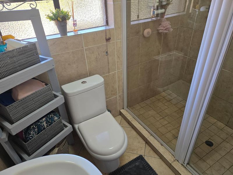 A functional bathroom featuring a glass-enclosed shower, a modern toilet, and neutral-toned wall and floor tiling.