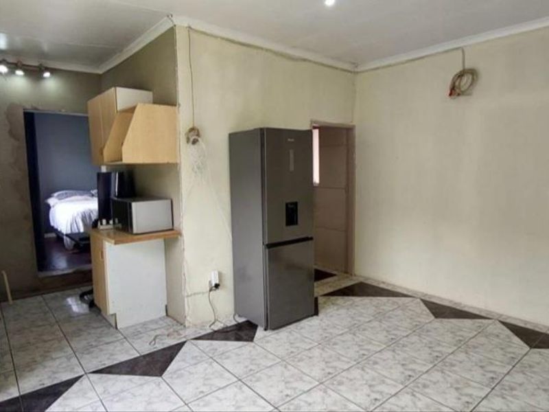 Open plan living and kitchen area featuring tiled flooring and basic cabinetry, requiring cosmetic updates and finishing to walls and electrical fixtures.