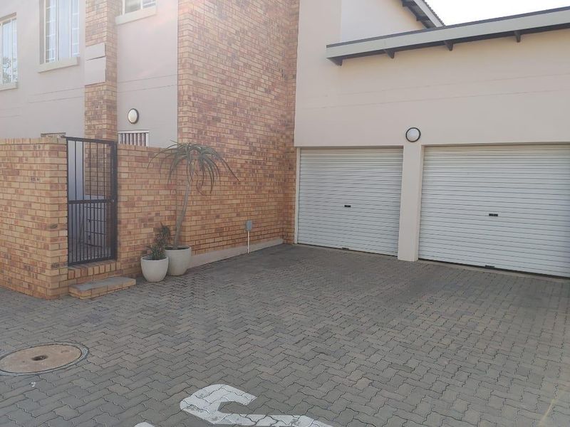 Front exterior view of a townhouse featuring a double garage, paved driveway, and brick facade detailing.