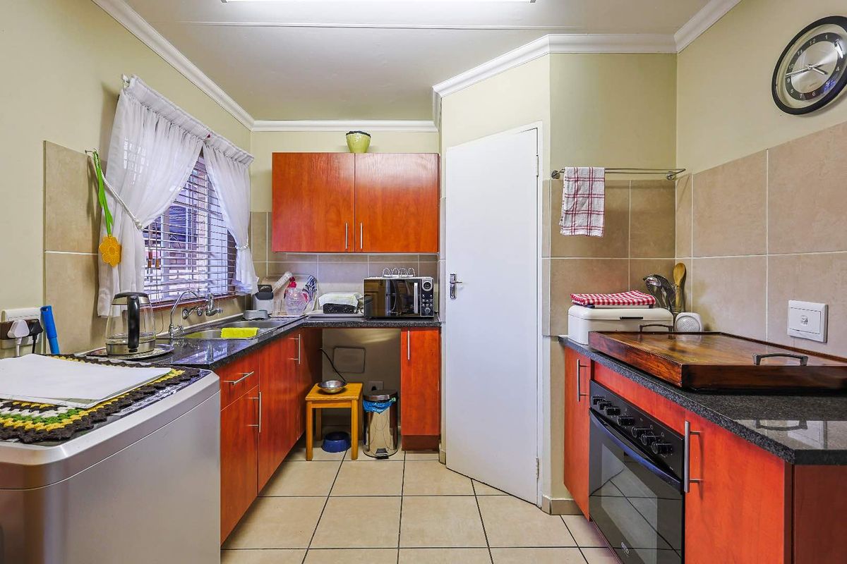 A functional kitchen featuring wood-finish cabinetry, granite countertops, tiled splashbacks, and a built-in oven with hob.