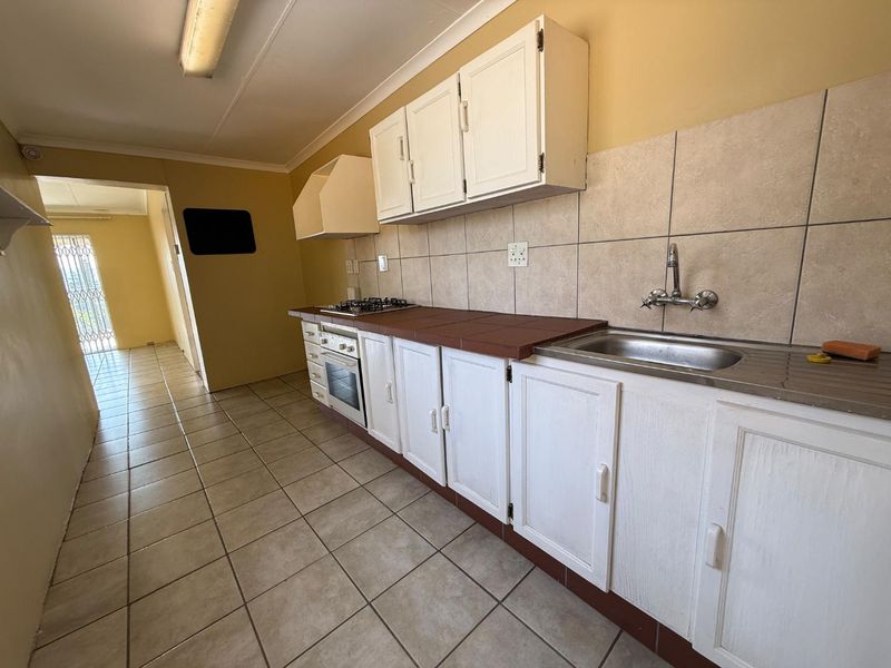 A functional kitchen featuring built-in cabinetry, a gas hob, an integrated oven, and tiled flooring, offering a blank canvas for potential modern updates.