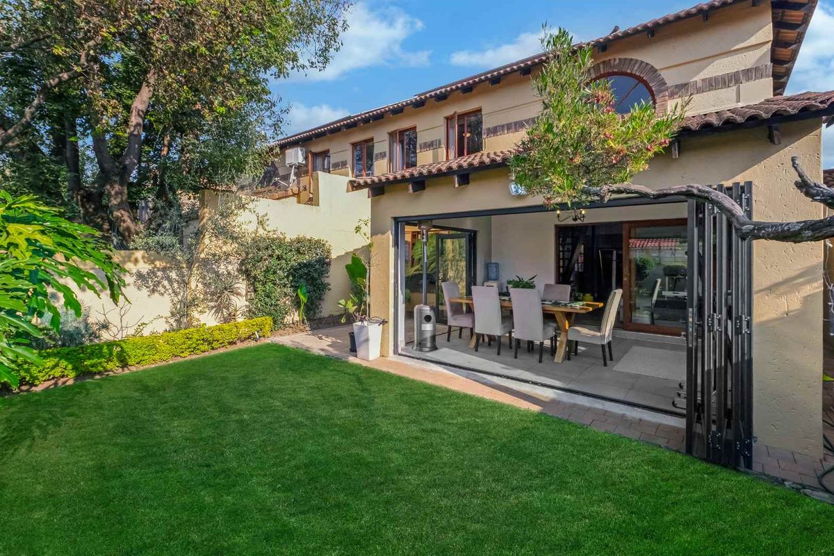 Rear view of the property featuring a well-maintained garden, paved patio, and large bi-fold doors providing seamless indoor-outdoor flow.