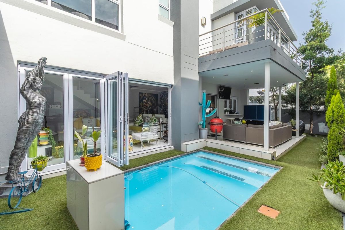 Rear view of the property featuring a swimming pool, covered patio area, and a balcony on the upper level with modern architectural finishes.