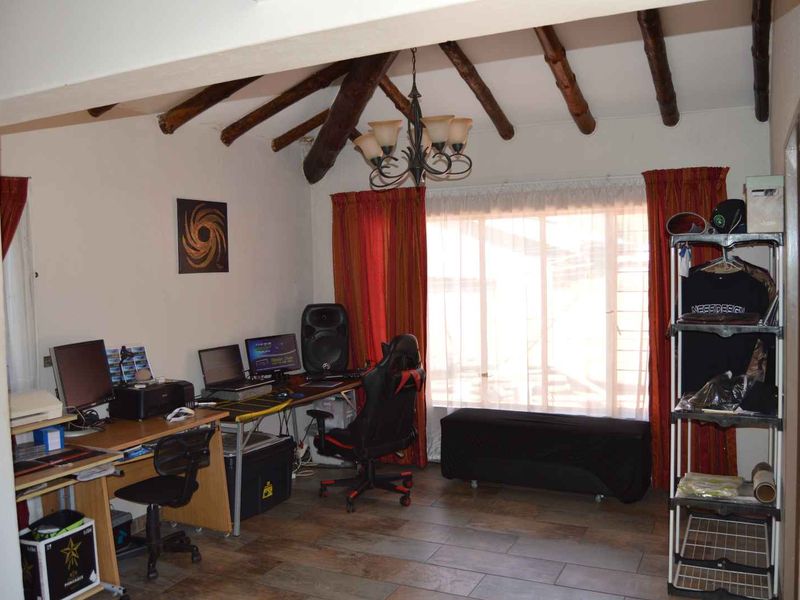A living area featuring exposed timber ceiling beams, tiled flooring, and a large window, currently utilized as a home office space.