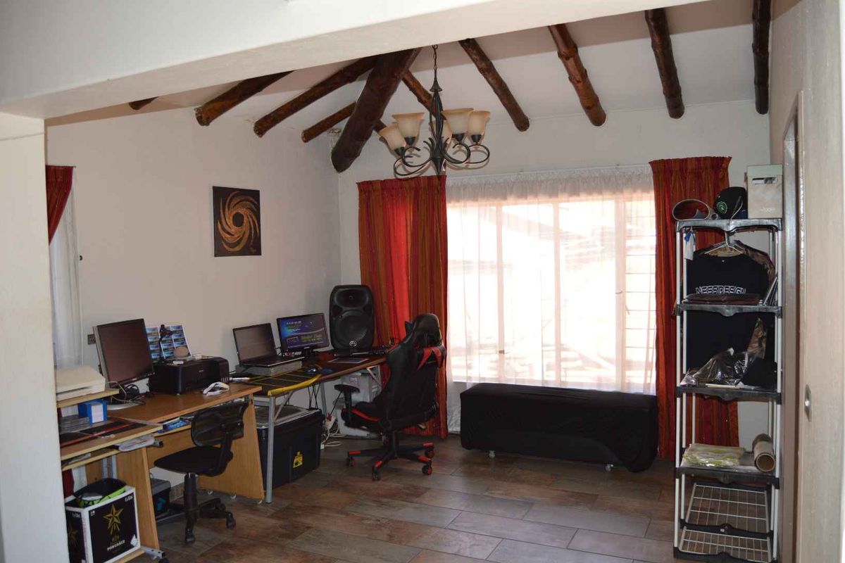 A living area featuring exposed timber ceiling beams, tiled flooring, and a large window, currently utilized as a home office space.