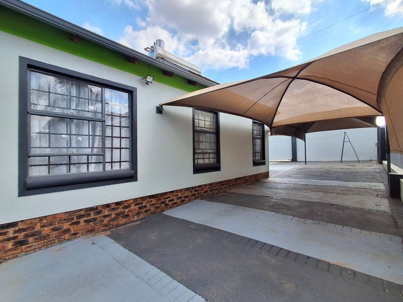 Exterior view of the property featuring a paved driveway, a large shade sail for parking, and a solar geyser installed on the roof.