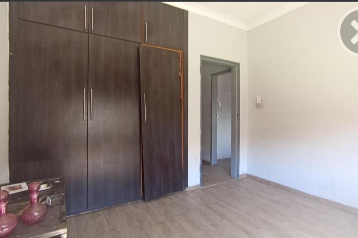 A bedroom featuring built-in dark wood-finish cupboards and tiled flooring, with a doorway leading to an adjacent hallway.