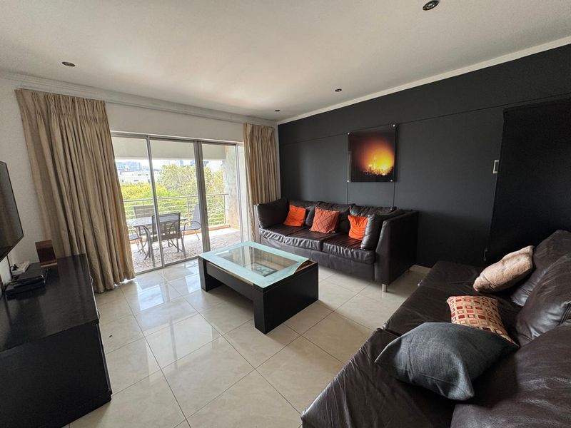Spacious living room featuring large sliding glass doors leading to a balcony, neutral tiled flooring, and a modern dark accent wall.